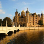 Das Schweriner Schloss mit seiner Brücke im goldenen Licht der Sonne, umgeben von Wasser.