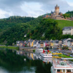 Blick auf Cochem an der Mosel mit der Reichsburg auf dem Hügel und Booten am Ufer.