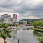 Blick auf die Saar in Saarbrücken mit modernen Gebäuden am Flussufer und bewölktem Himmel.