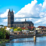 Blick auf den Magdeburger Dom und die historische Hubbrücke über die Elbe bei blauem Himmel.