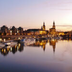 Dresdner Altstadt an der Elbe bei Sonnenuntergang mit reflektierenden Lichtern im Wasser.