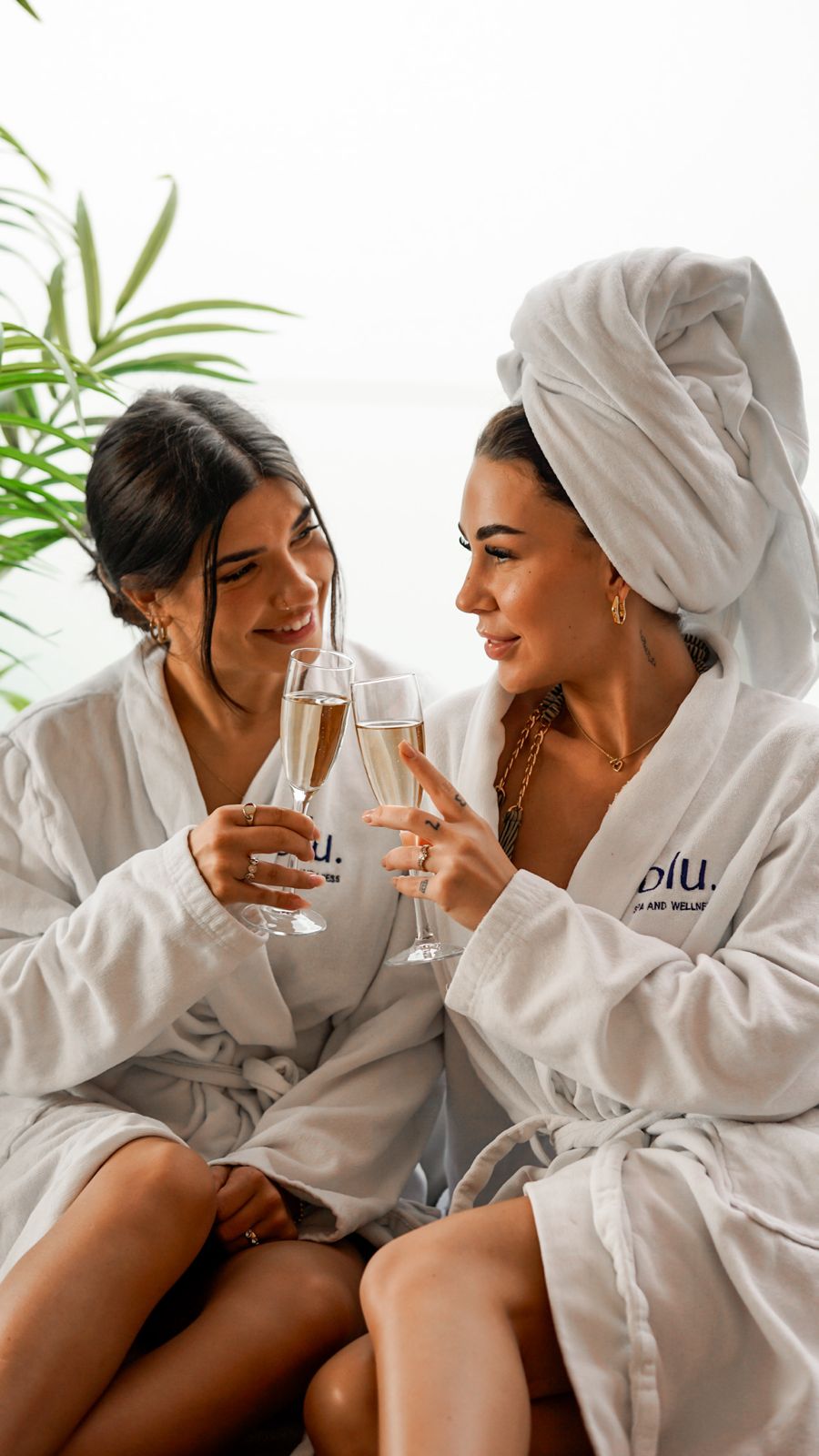 Zwei Freundinnen stoßen im BLU Spa Dortmund in Bademänteln mit Champagnergläsern an.