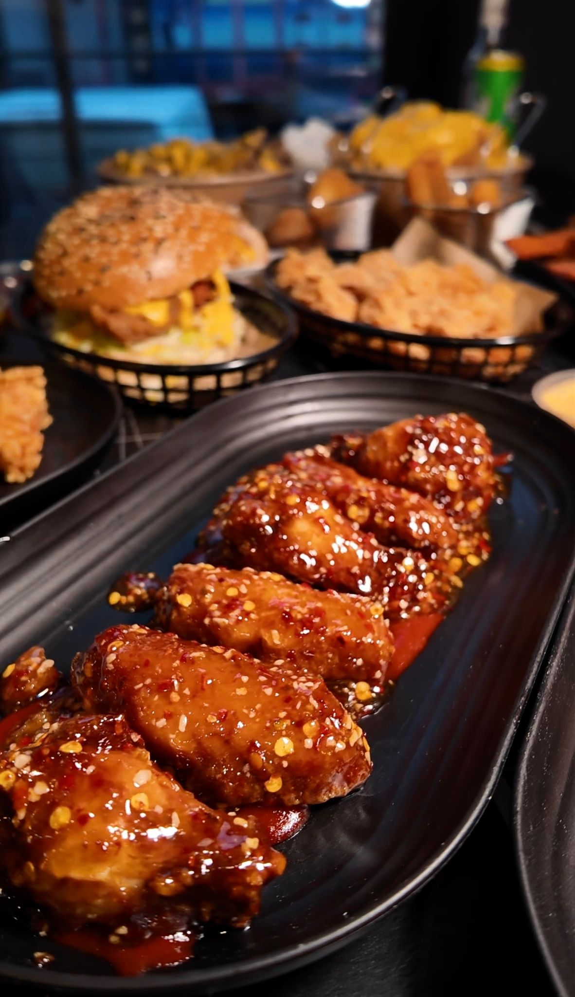 Glasierte BBQ-Chicken-Wings im Vordergrund mit Burger und weiteren Beilagen im Hintergrund im Chickenhood Datteln