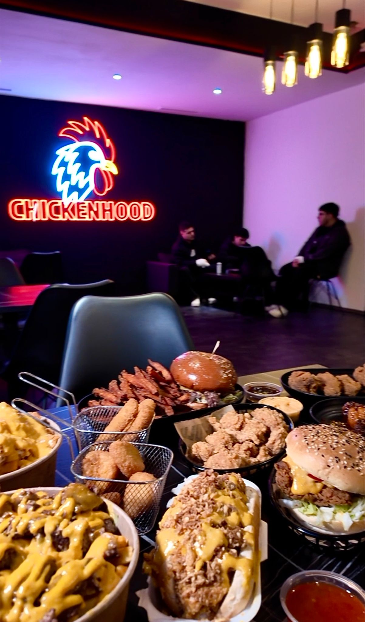 Tisch mit Chickenhood-Spezialitäten im Vordergrund und Gäste im Innenbereich