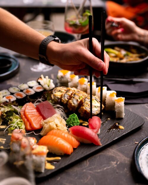 Hand greift mit Stäbchen nach Sushi auf einer bunt gemischten Platte im Oishinbo Dortmund