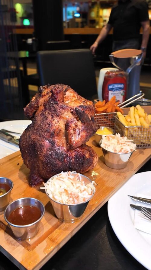 Knusprig gegrilltes Hähnchen auf einem Holzbrett serviert mit Krautsalat, Pommes, Süßkartoffelpommes und Saucen
