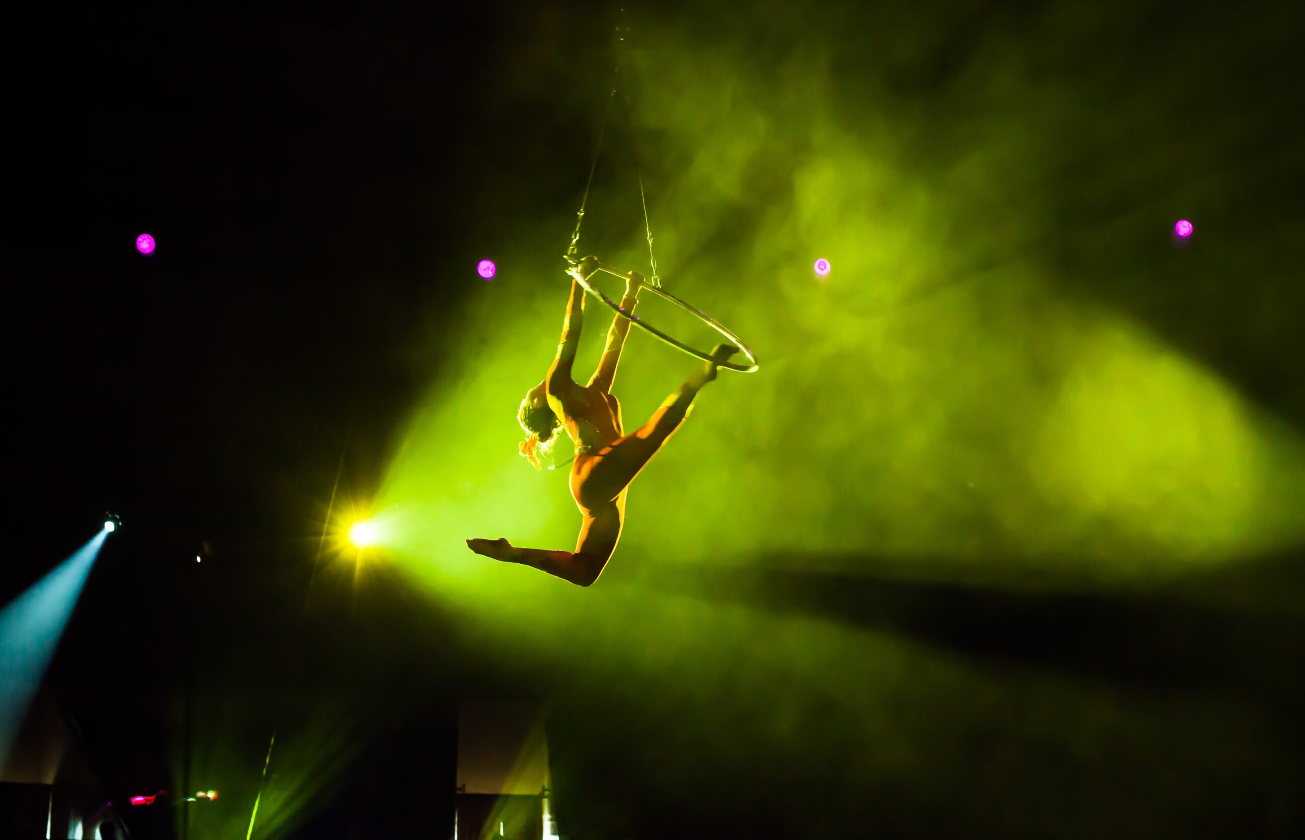 Luftakrobatin am Aerial Hoop im grünen Showlicht während einer Performance