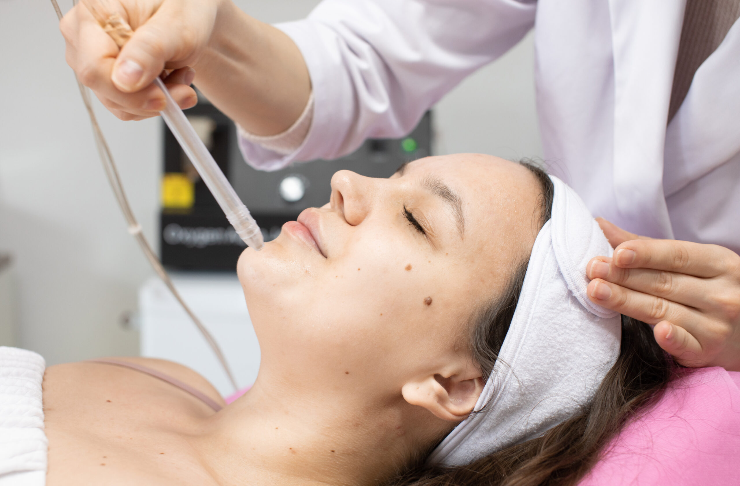 Frau mit Stirnband liegt entspannt auf der Behandlungsliege und erhält eine Aqua Facial Anwendung mit transparentem Handstück zur porentiefen Reinigung