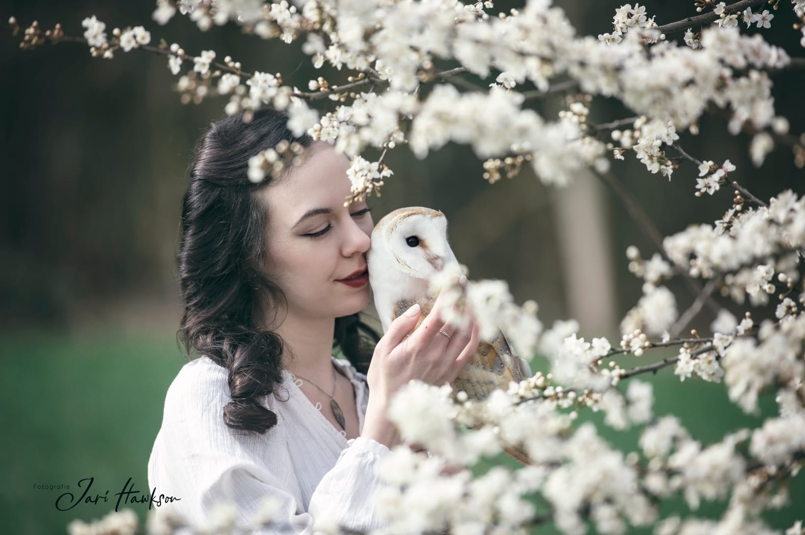 Frau mit Schleiereule inmitten blühender Äste bei der Falknerei Skyhunters in Frechen