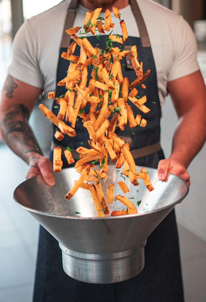 Frische Pommes werden in einer Metallschüssel hochgeworfen, zubereitet von einem Koch der Frittenküche Dortmund