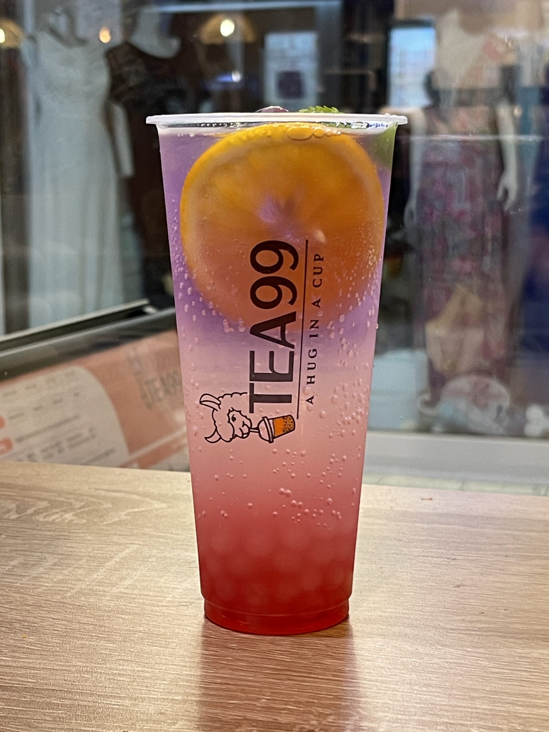 Fruchtiger Bubble Tea mit Orangenscheibe von Tea99 Frankfurt auf einem Holztisch im Laden