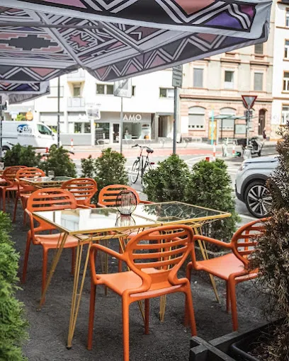 Außensitzbereich des African Violet Frankfurt mit orangefarbenen Stühlen, Glasplatten-Tischen und dekorativem Sonnenschutz im afrikanischen Musterstil