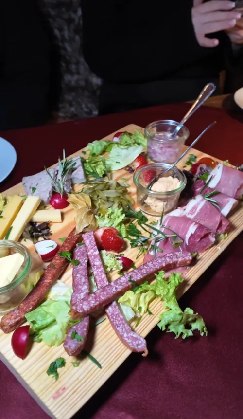 ustikale Brettljause in der Alm Fernweh mit verschiedenen Wurst- und Käsesorten, Aufstrichen, Radieschen, Trauben, Erdbeeren und frischen Kräutern auf Holzbrett serviert