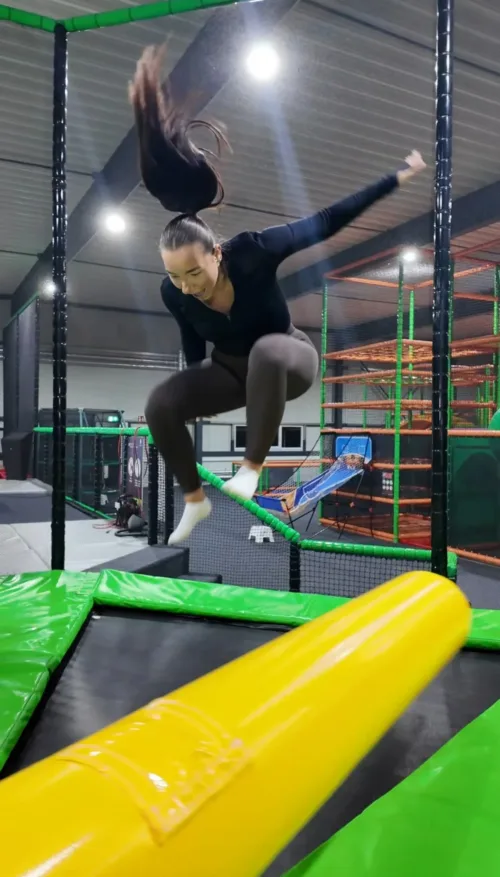 Frau springt in einem Trampolinpark über ein rotierendes Hindernis im FunFusion Wetzlar, Action und Geschicklichkeit in moderner Indoor-Arena