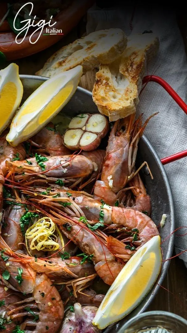 Italienisches Meeresfrüchtegericht mit Garnelen, Zitronenspalten, Knoblauch und geröstetem Brot in einer rustikalen Pfanne im Gigi Italian Köln