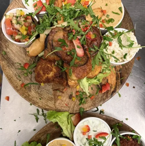 Tapasplatte mit nepalesischen Spezialitäten aus dem Hamro Nepali Restaurant Frankfurt, darunter Pakora, Dips, Chutneys, Salate und Joghurt, serviert auf rustikalem Holzbrett