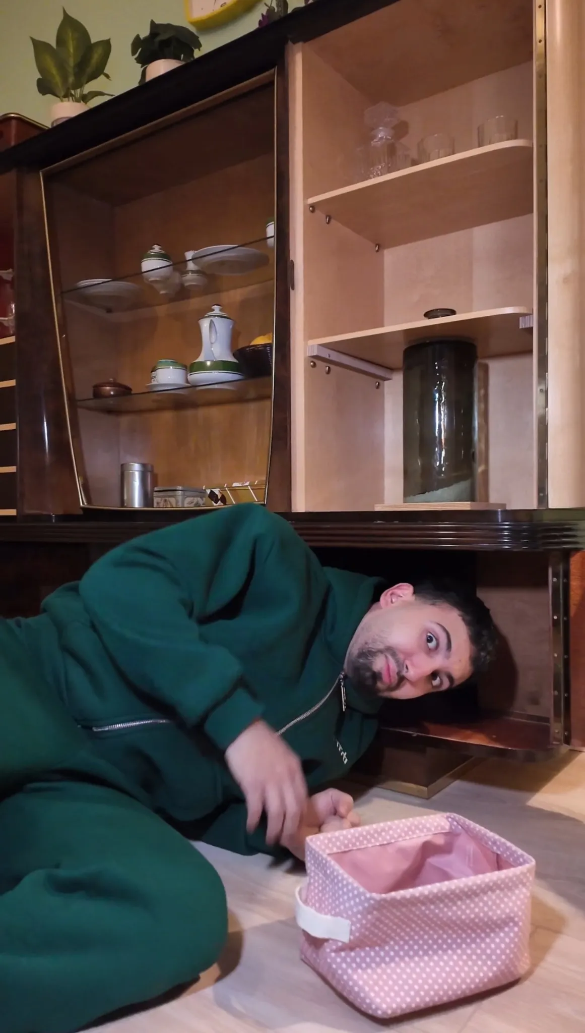 Teilnehmer im Escape Room „Muriel_Ingrid“ liegt lachend unter einem alten Wohnzimmerschrank und entdeckt ein geheimes Fach im Retro-Möbelstück