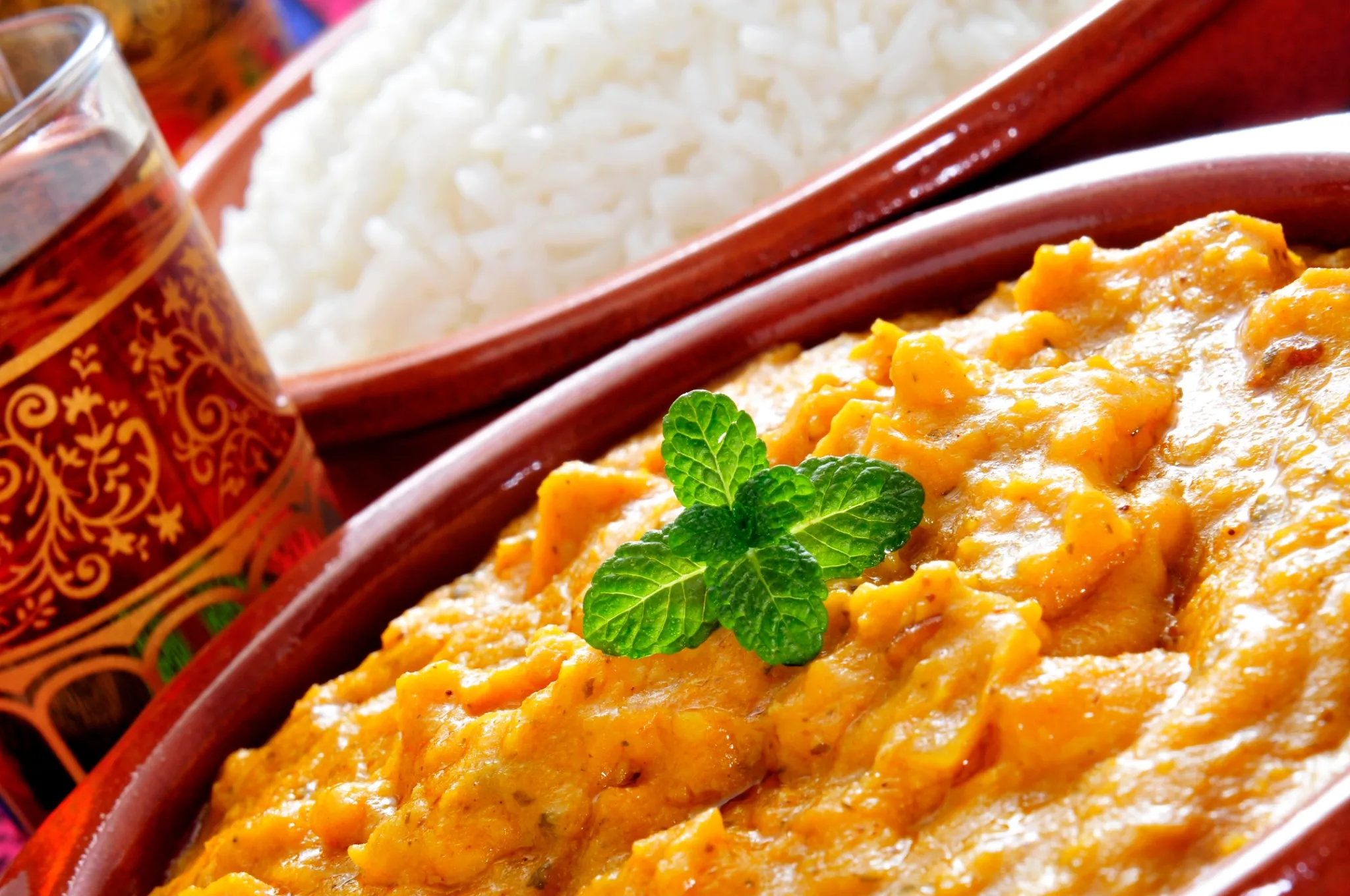 Cremiges indisches Dal aus gelben Linsen in einer Tonschale, garniert mit frischer Minze, dazu eine Schale Reis im Hintergrund