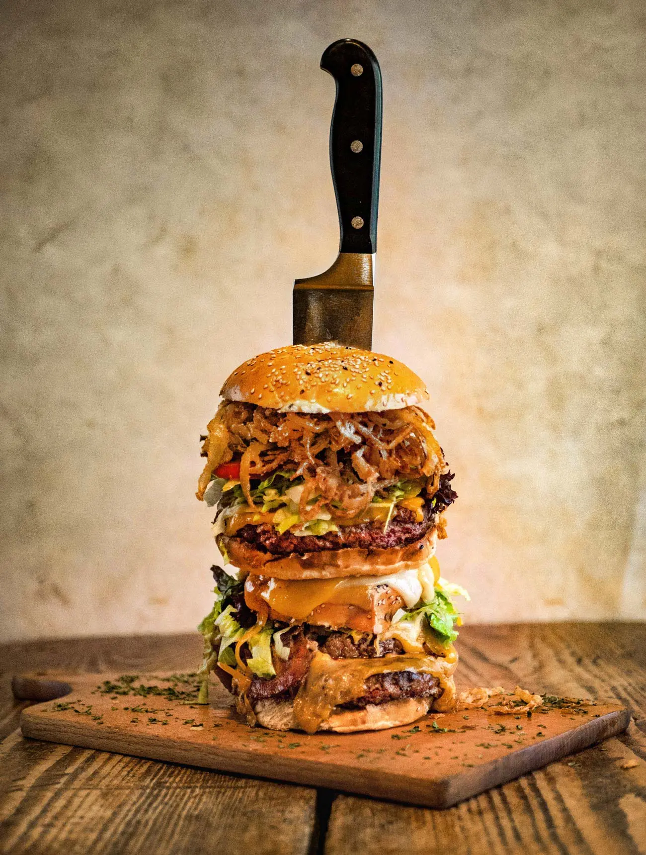XXL-Burger aus dem Red Barn BBQ Restaurant mit mehreren Lagen Fleisch, Käse, Salat, Zwiebeln und BBQ-Sauce, fixiert mit einem großen Messer im Bun