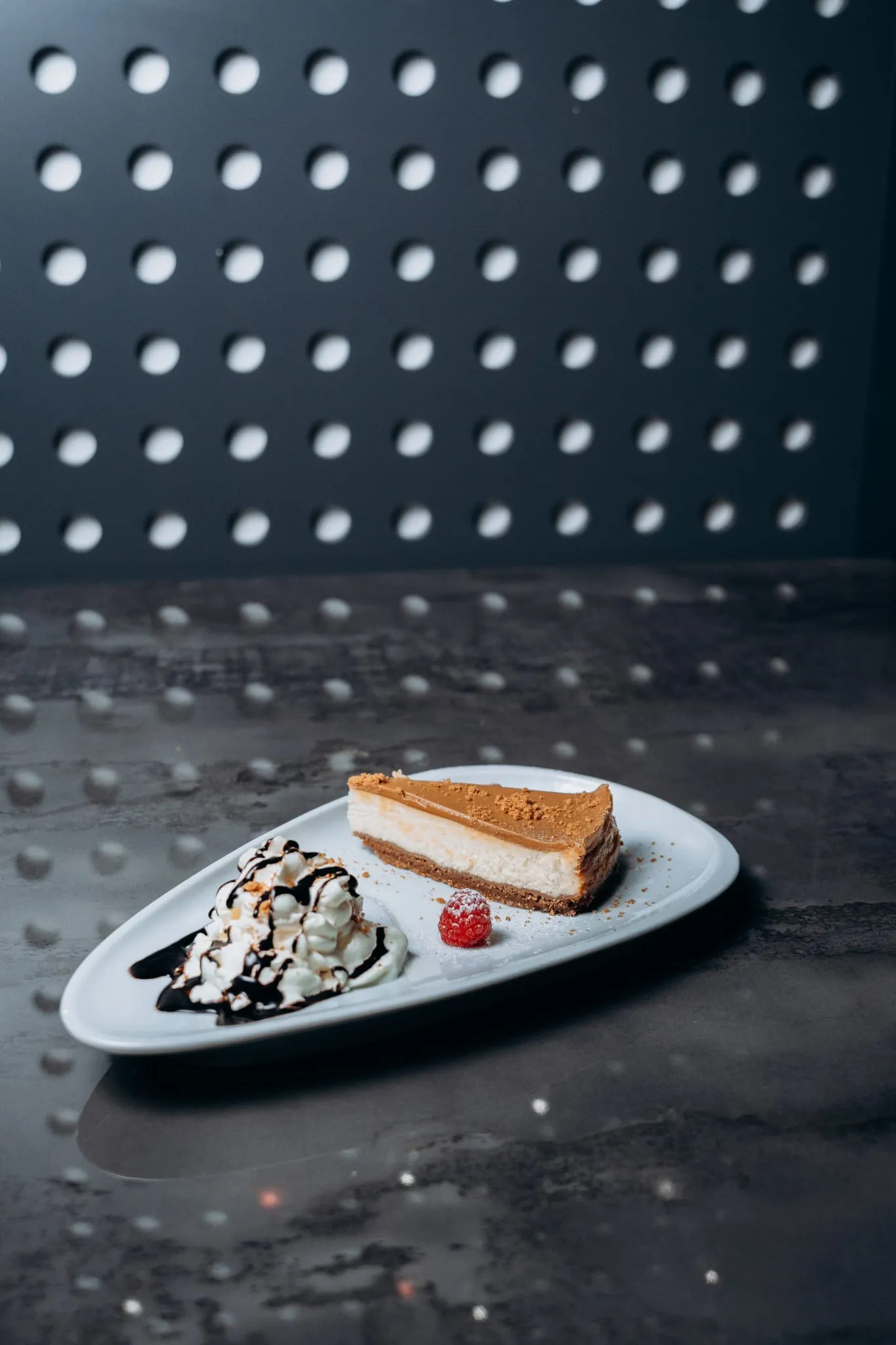 Dessertteller mit Cheesecake, einer Kugel Vanilleeis mit Schokosauce, Sahne und Himbeere, stilvoll angerichtet auf moderner Platte im Shiva Food and More Dinslaken