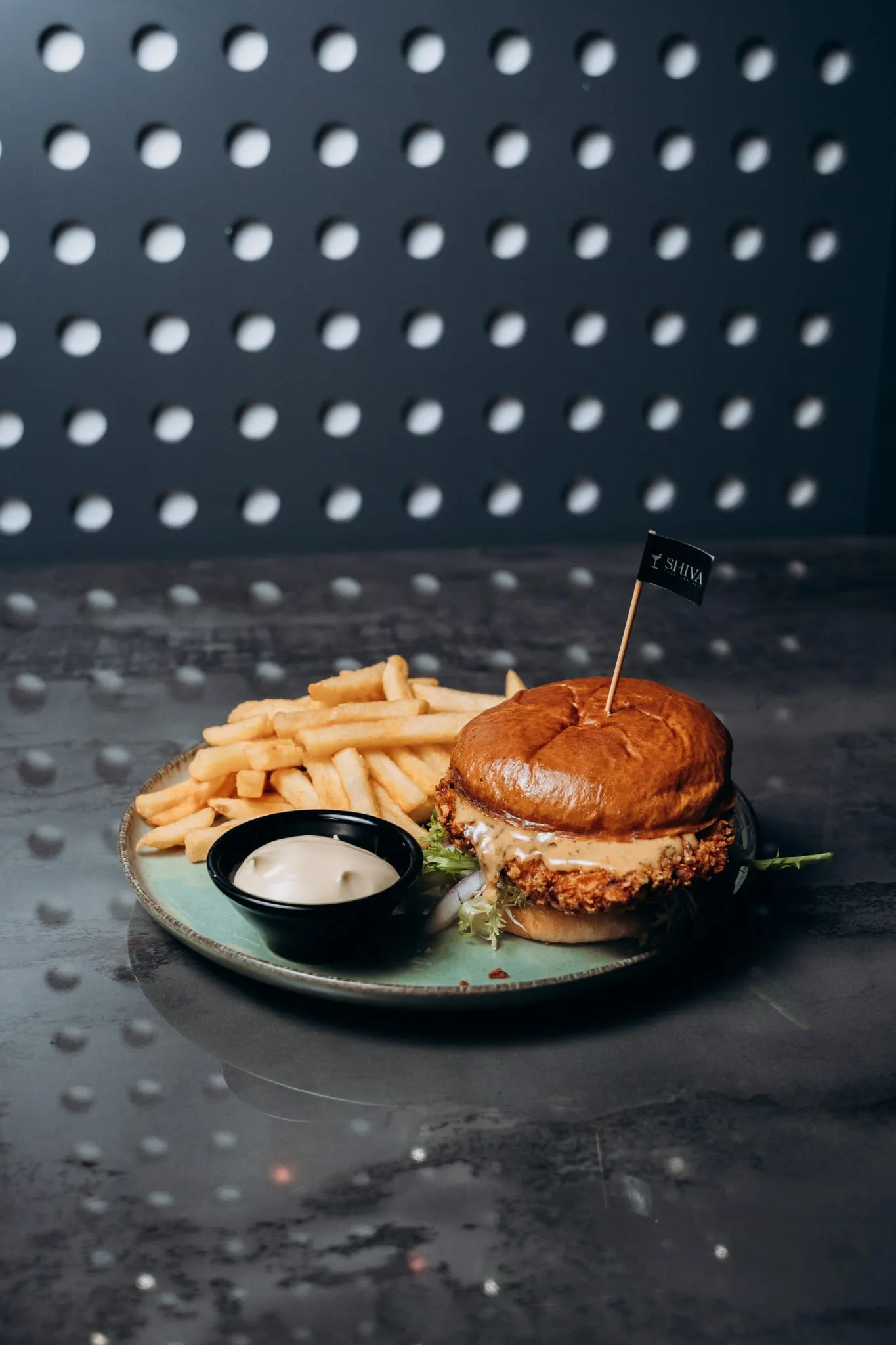 chicken-Burger mit knusprigem Patty, Salat und Sauce im Brioche-Bun, serviert mit Pommes und Dip auf einem Teller im Shiva Food and More Dinslaken