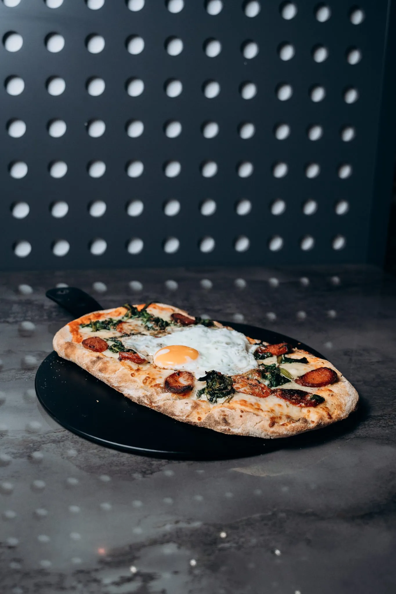 fenfrische Pinsa vom Shiva Food and More Dinslaken, belegt mit Ei, Spinat und Käse, serviert auf schwarzem Teller im modernen Ambiente