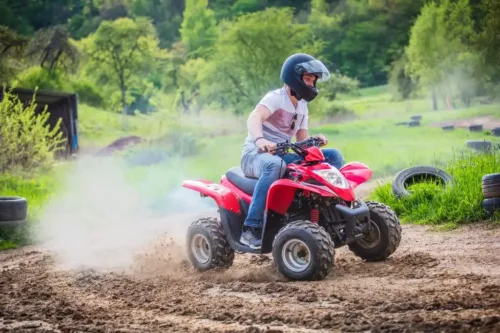 Mann fährt mit rotem Quad über eine staubige Offroad-Strecke inmitten grüner Natur