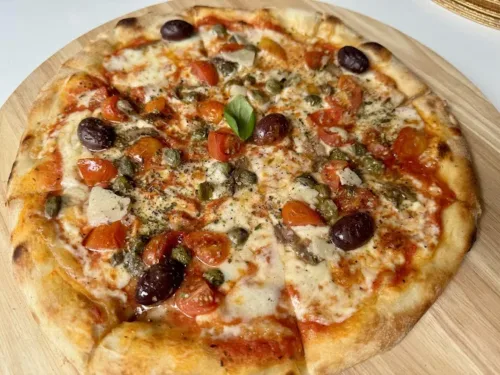 Pizza aus dem Spaccanapoli Da Enzo Essen mit Tomaten, Kapern, schwarzen Oliven, Basilikum und Oregano auf Holzbrett serviert