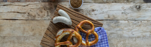 Traditionelles bayerisches Frühstück mit Weißwurst, Brezeln und süßem Senf auf Holzbrett
