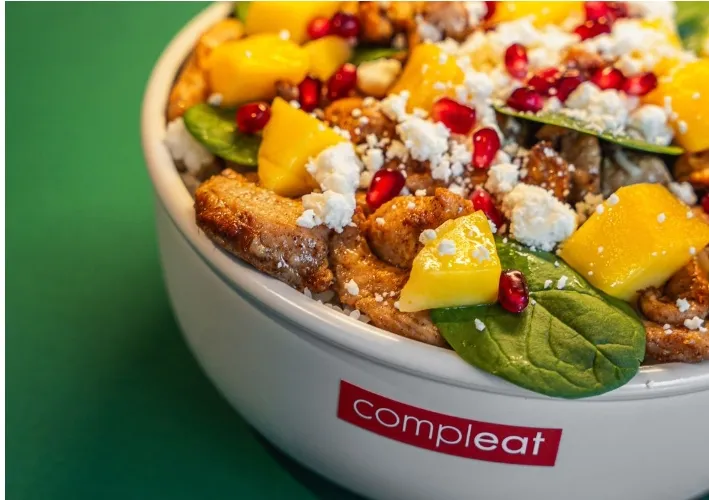 Frische Bowl von Compleat Nordend mit Hähnchen, Mango, Granatapfelkernen, Spinat und Feta in einer weißen Schüssel