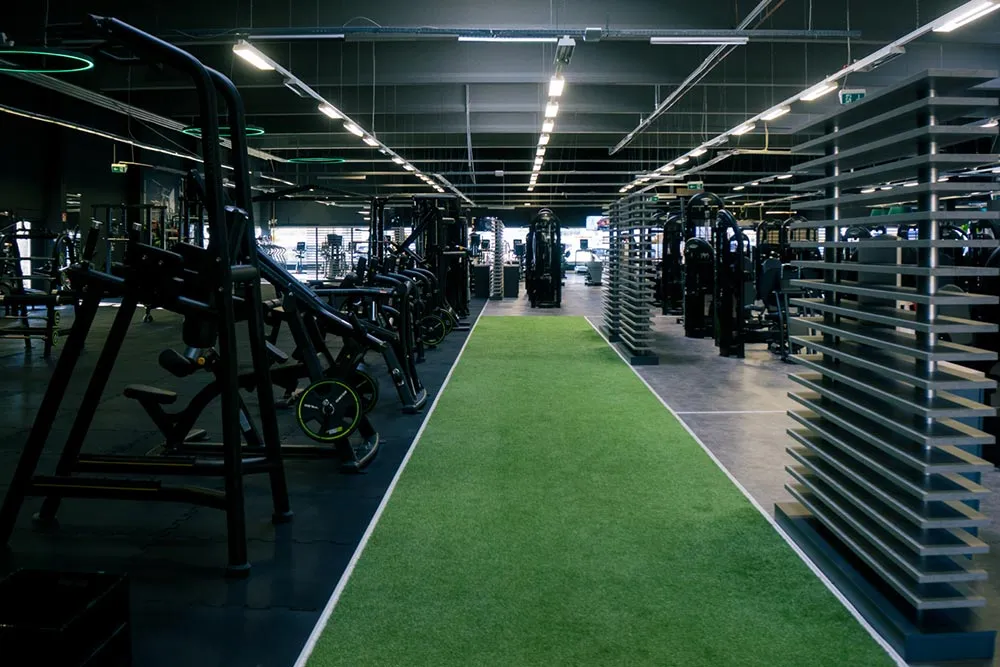 Fitnessstudio mit grüner Kunstrasenlaufbahn und Trainingsgeräten an den Seiten