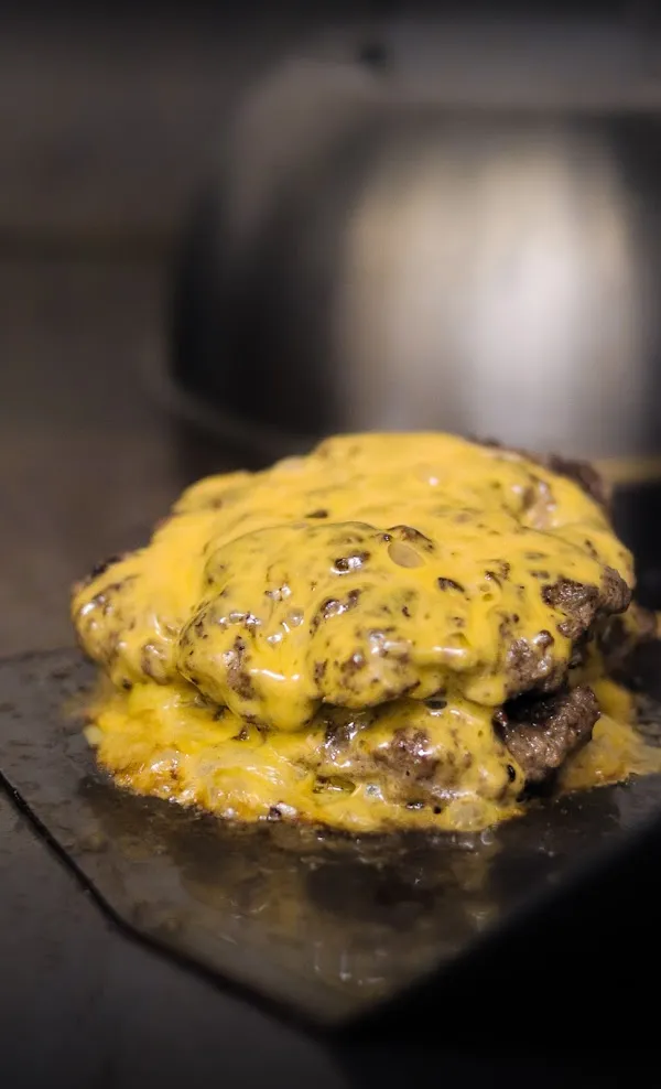 Zwei saftige Burgerpatties mit geschmolzenem Käse auf der Grillplatte in Nahaufnahme