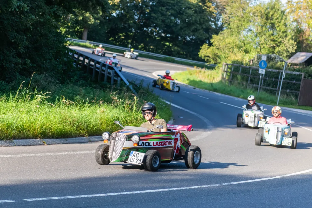 Mehrere Hotrods fahren im Konvoi durch eine kurvige Landstraße bei sonnigem Wetter während der Hotrod Tour Aachen