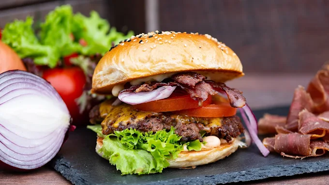 Saftiger Bacon-Cheeseburger mit Salat, Tomate, Zwiebeln und Käse im Sesambrötchen