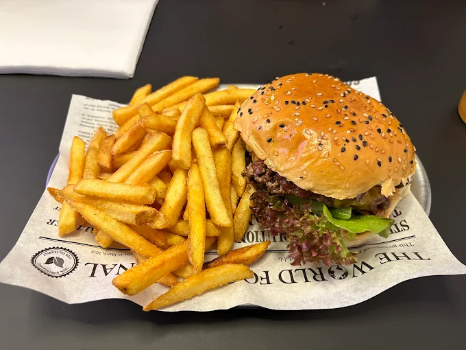 Klassischer Cheeseburger mit Salat und Pommes auf Papier im Streetfood-Stil serviert