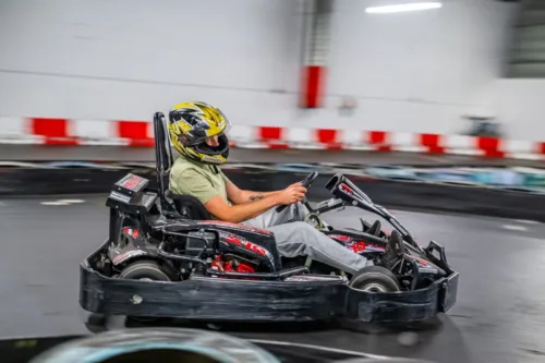Fahrer mit gelb-schwarzem Helm fährt in einem roten Rennkart mit hoher Geschwindigkeit auf der Indoor-Kartbahn Hungen