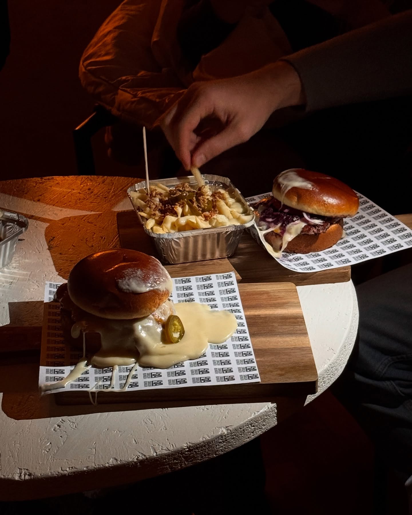Zwei Smash Burger und Loaded Fries auf Tabletts, Hand greift nach Pommes