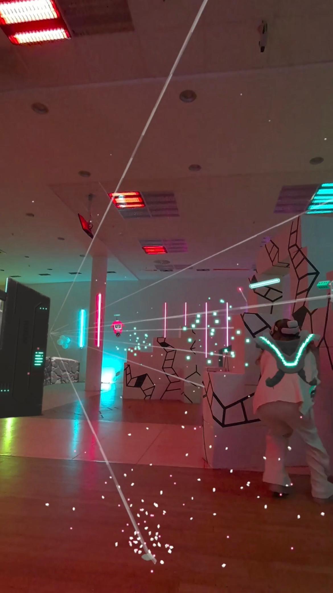 Person in VR-Ausrüstung weicht virtuellen Lasern in futuristischer Spielarena in Berlin aus.