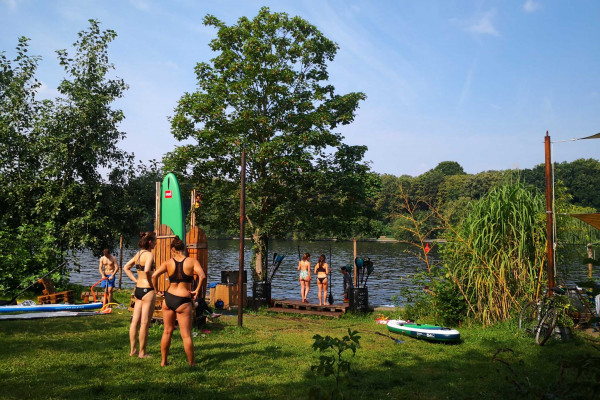 Menschen bereiten sich mit SUP-Boards am Seeufer im Grünen auf das Stand-Up-Paddling vor