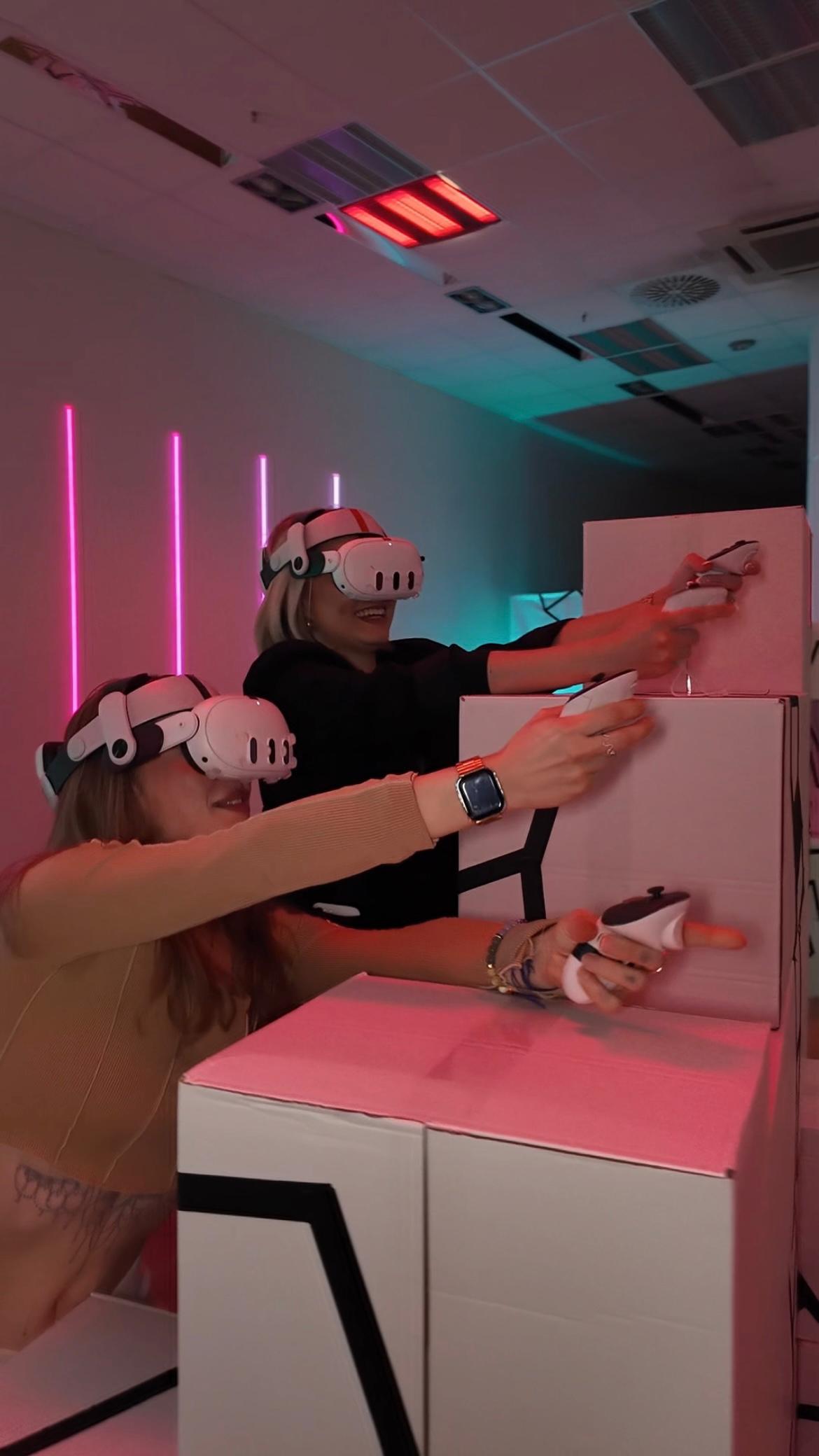 Zwei Frauen spielen mit VR-Brillen und Controllern in einer futuristischen Free-Roam-Arena in Berlin.