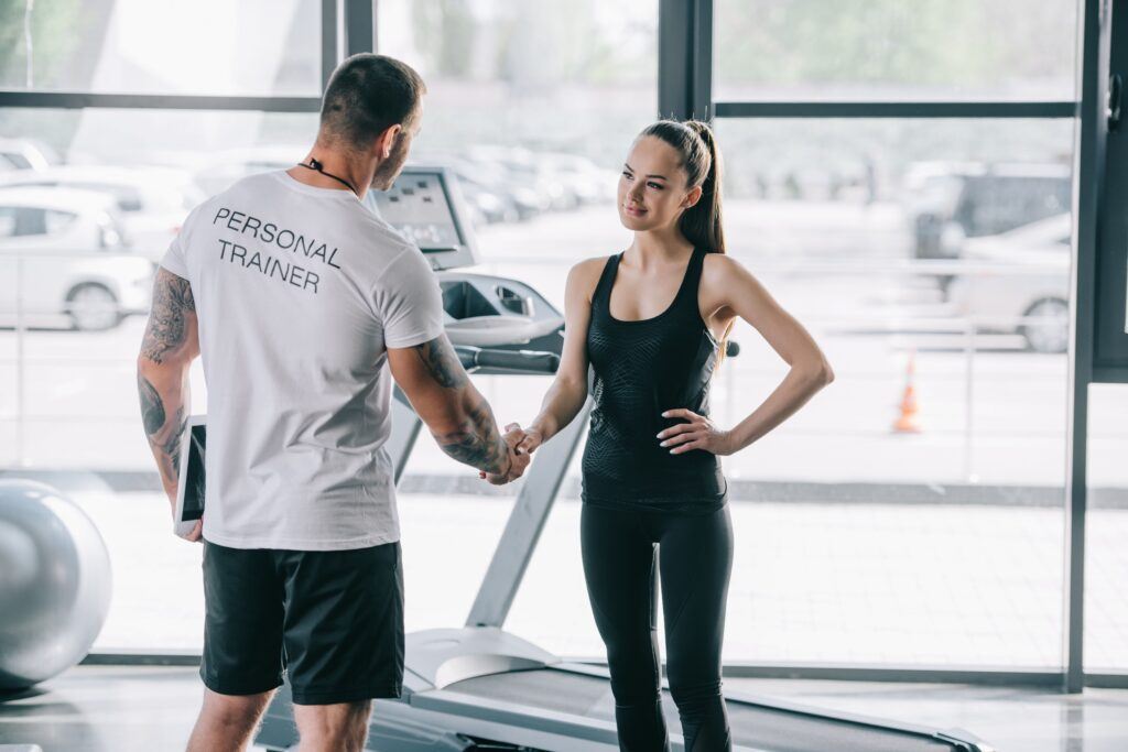 Fitnessstudio-Szene mit Personal Trainer und Kundin beim Handschlag vor dem Trainingsstart