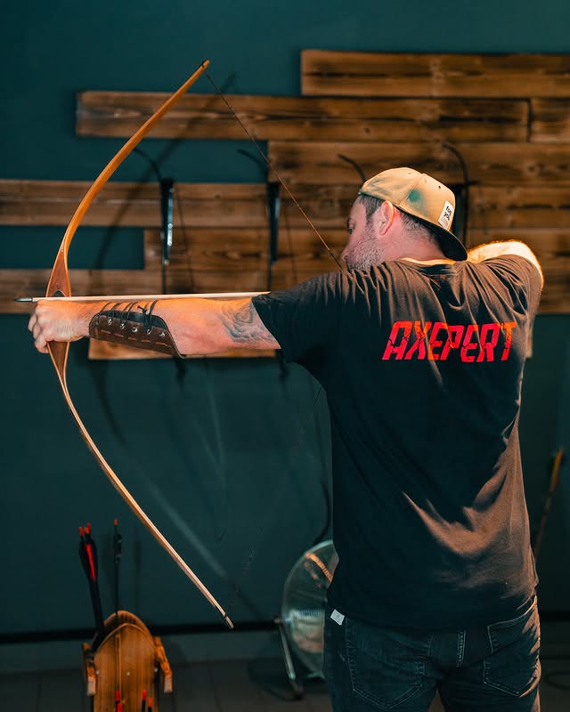 Teilnehmer beim Bogenschießen mit gespanntem Bogen und Schutzarmband in der Halle von Rage Axe Weiterstadt