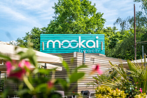 Mookai Beach Logo an der Außenwand des Lokals in Rodenbach, umgeben von Pflanzen