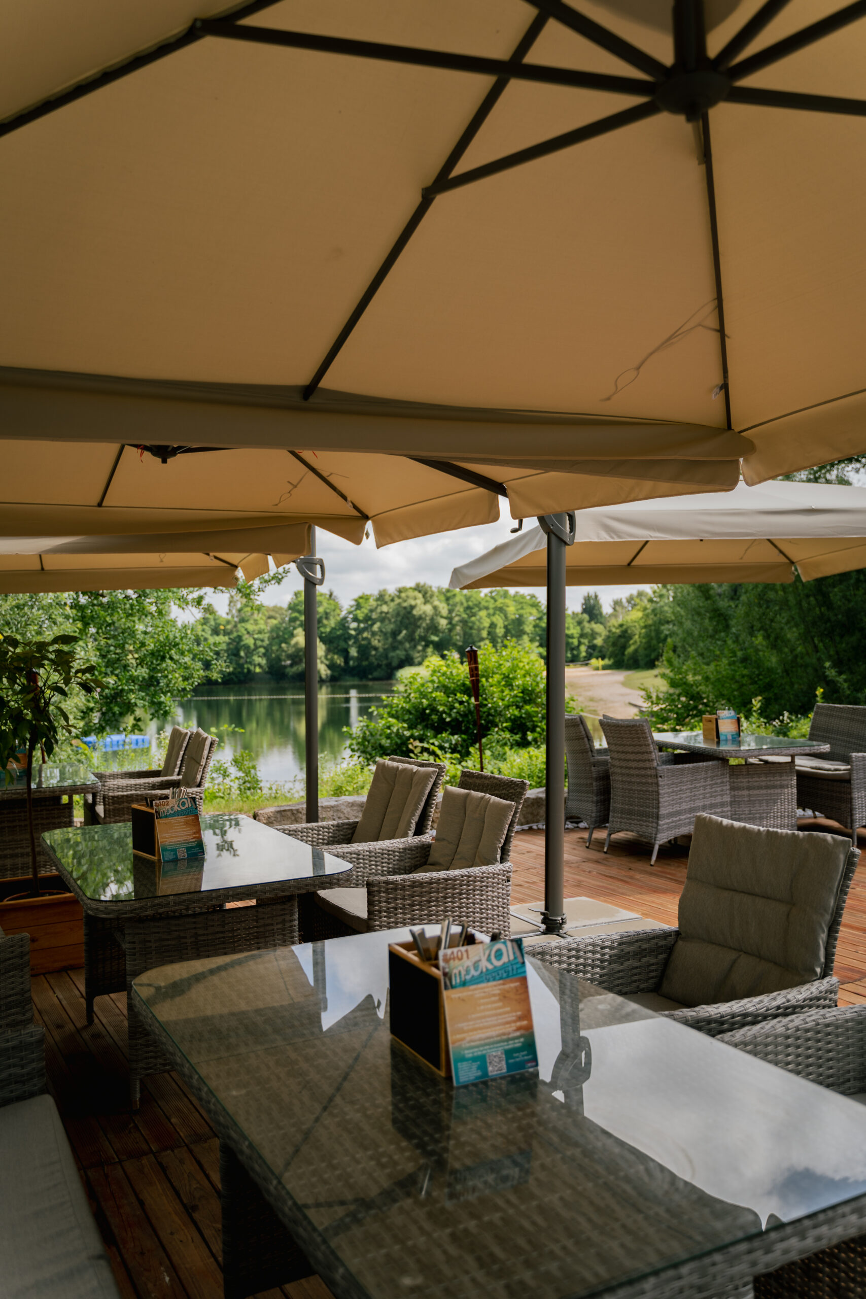 Terrasse mit Blick auf den See im Mookai Beach Rodenbach, ausgestattet mit Sonnenschirmen und bequemen Sitzplätzen