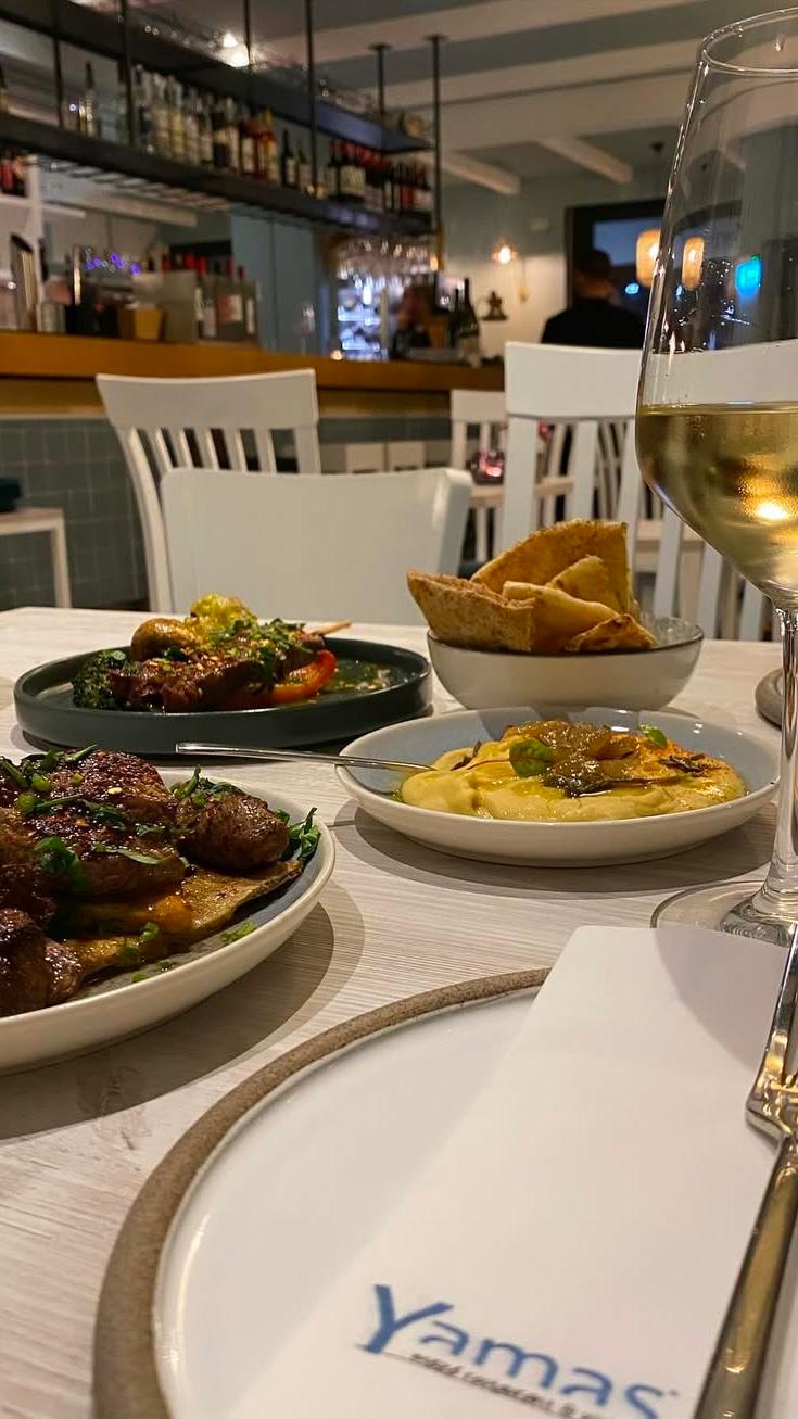 Meze-Teller mit gegrilltem Fleisch, Beilagen und einem Glas Weißwein bei Yamas Dortmund